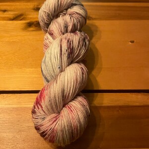 Könnte beinhalten: Eine Garnrolle in Cremefarbe mit roten und blauen Sprenkeln. Das Garn ist zu einer Kugel gewickelt.