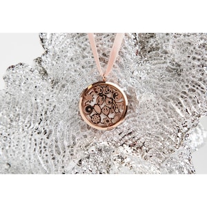以下が含まれることがあります： 様々な宗教や文化のシンボルが刻まれた円形のチャームが付いた、ローズゴールドのペンダントネックレス。チャームは繊細な透かし模様で囲まれています。