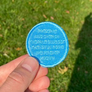 Puede incluir: Un parche redondo azul con texto bordado en blanco que dice "Preserve and Cherish the Pale Blue Dot, the Only Home We've Ever Known."