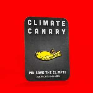 Puede incluir: Un pin de esmalte negro y blanco con un canario amarillo acostado de espaldas. El pin dice "Climate Canary" y "Pin Save The Climate. All Profits Donated."