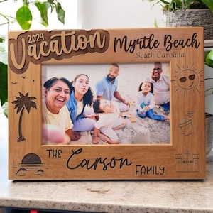 May include: A wooden photo frame with a carved design of a palm tree, sun, and sandcastle. The frame has the text "Vacation Myrtle Beach South Carolina 2024 The Carson Family" carved into it. A photo of a family is in the frame.