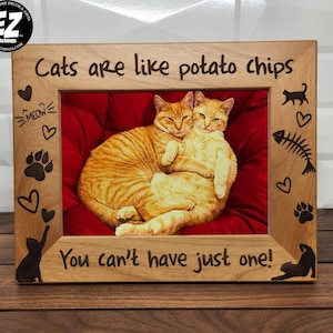 May include: A wooden picture frame with the text "Cats are like potato chips You can't have just one!" and a photo of two orange tabby cats cuddling. The frame is decorated with paw prints, hearts, and a fish bone.