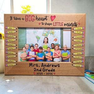 May include: A wooden picture frame with the text "It takes a BIG heart to shape LITTLE minds." The frame includes a photo of a teacher and students. The frame also has the names of the students on the sides.