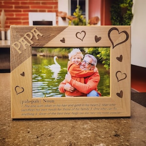 May include: A wooden picture frame with a carved inscription that reads "PAPA" and a definition of the word "papa" below the photo. The photo shows a man and a child hugging in front of a lake.