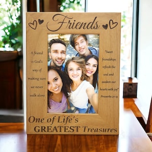 May include: Wooden picture frame with the word "Friends" and heart designs engraved at the top. The frame holds a photo of five smiling people. Text on the frame includes quotes about friendship and the phrase "One of Life's GREATEST Treasures."