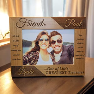 May include: A wooden picture frame with a photo of two people smiling. The frame is engraved with the words "Friends", "Paul", "Linda", and "...One of Life's GREATEST Treasures". The frame also includes a quote about friendship from Proverbs 27:9.