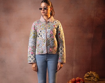 Peut inclure: Veste matelassée bleu clair à motifs floraux, portée avec un jean bleu clair et des bottes noires. La veste a une bordure rayée rose et blanche. Un panier d'oranges et des caisses en bois sont en arrière-plan. La veste mesure environ 60 cm de long.