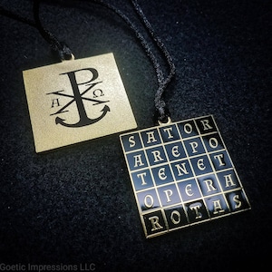Puede incluir: Dos colgantes de color dorado en cordones negros. El primer colgante presenta un ancla negra con las letras "A", "P", "Q" y "Ω" alrededor. El segundo colgante es un cuadrado negro con un borde dorado y las letras "SATOR AREPO TENET OPERA ROTAS" dispuestas en un cuadrado.