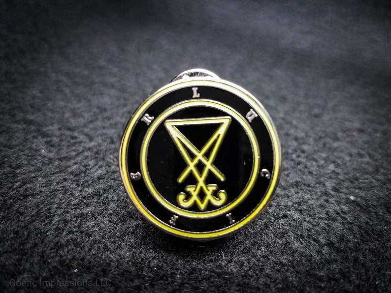 Puede incluir: Un pin de esmalte negro y amarillo con un sigilo dentro de un c&iacute;rculo. El sigilo es un pentagrama con una cruz en su interior. El c&iacute;rculo tiene las letras L, W, I, C, R y S alrededor del exterior.