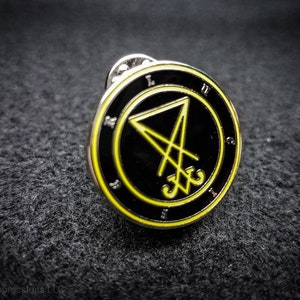 Puede incluir: Un pin de esmalte negro y amarillo con un pentagrama y el texto "LXV" dentro de un c&iacute;rculo.