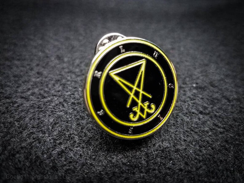 Puede incluir: Un pin de esmalte negro y amarillo con un pentagrama y el texto "LXV" dentro de un c&iacute;rculo.