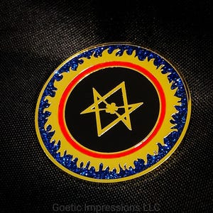 May include: A circular pin with a black centre featuring a yellow star-like design. The pin has a red inner ring, a yellow outer ring with flame-like edges, and a blue glitter border. The text "Goetic Impressions LLC" is at the bottom.
