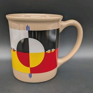 Puede incluir: Taza de cerámica color beige con un asa grande. La taza presenta un diseño geométrico colorido con secciones blancas, negras, amarillas y rojas. El diseño incluye un círculo central y líneas verticales. Adecuada para bebidas frías o calientes.
