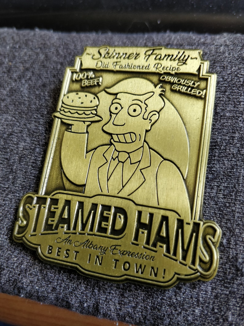 May include: A gold-colored metal sign with the text "Skinner Family Old Fashioned Recipe" and "Steamed Hams An Albany Expression BEST IN TOWN!" The sign features a cartoon character holding a hamburger with the text "100% BEEF!" and "OBVIOUSLY GRILLED!"
