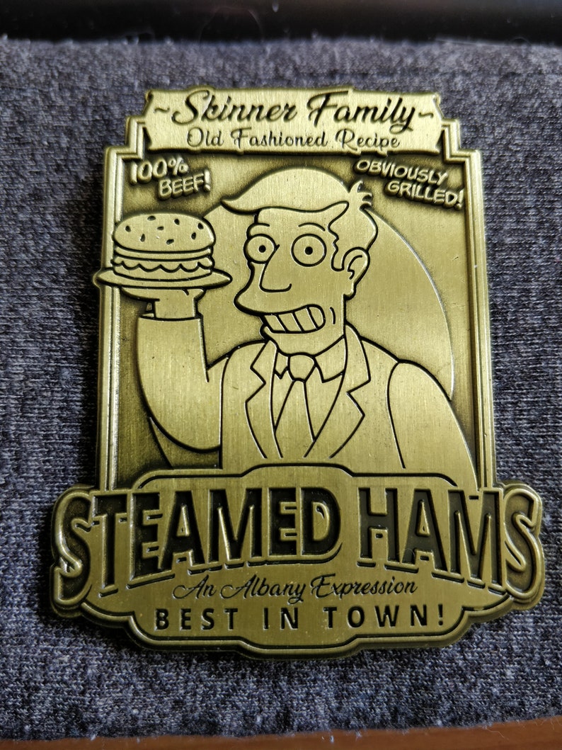 May include: A gold-colored metal sign with the text "Skinner Family - Old Fashioned Recipe" and "Steamed Hams - An Albany Expression - Best in Town!"  The sign features a cartoon image of a man holding a hamburger with the text "100% Beef!" and "Obviously Grilled!"