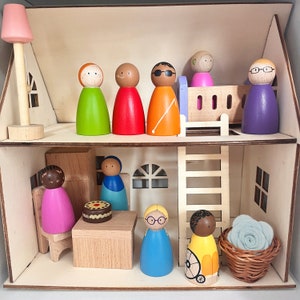 Op de afbeelding: Een houten poppenhuis met een verscheidenheid aan houten poppen, waaronder een pop met een roze jurk, een pop met een blauwe jurk, een pop met een gele jurk, een pop met een rode jurk, een pop met een groene jurk, een pop met een oranje jurk, een pop met een paarse jurk en een pop met een blauwe jurk. Het poppenhuis heeft een ladder, een bed en een tafel met een taart erop.