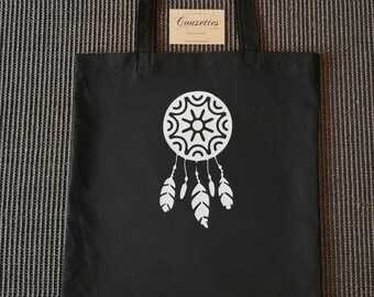 May include: Black canvas tote bag with a white dreamcatcher design. The bag has two black handles and a white label with the text "Cousettes".