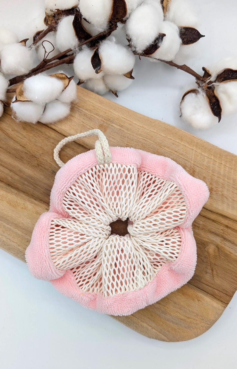 Puede incluir: Un puf de ba&ntilde;o de malla rosa y blanco con cierre de cord&oacute;n. El puf est&aacute; sobre una superficie de madera.