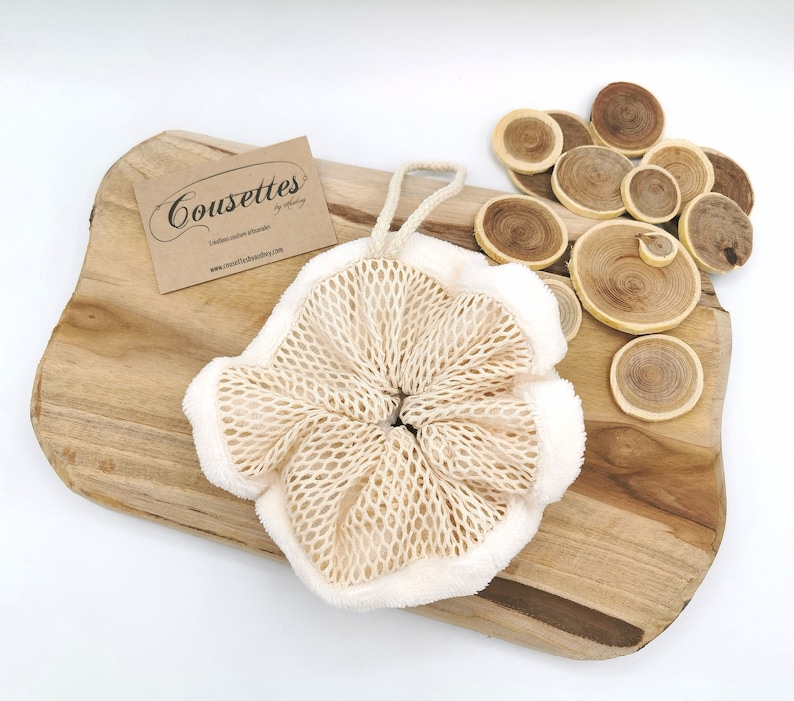 Puede incluir: Un puff de ba&ntilde;o blanco y beige con textura de malla y cierre de cord&oacute;n. El puff est&aacute; sobre una superficie de madera con discos de madera.