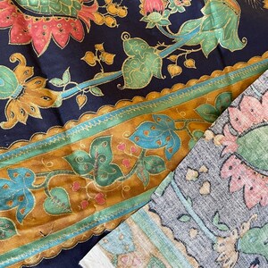 May include: A close-up of two fabric swatches with a floral pattern. The top swatch is a dark blue fabric with gold, green, and pink floral designs. The bottom swatch is a light gray fabric with a brown, green, and pink floral design.