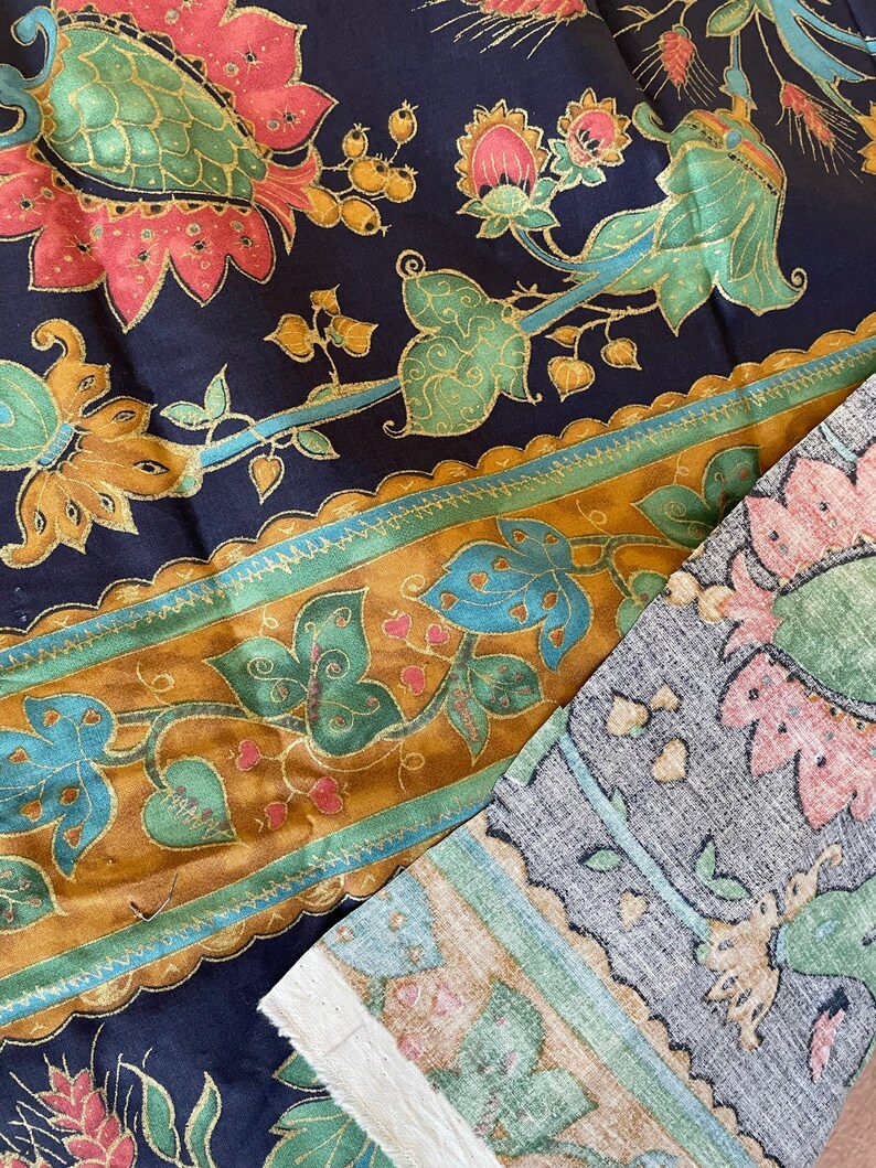 May include: A close-up of two fabric swatches with a floral pattern. The top swatch is a dark blue fabric with gold, green, and pink floral designs. The bottom swatch is a light gray fabric with a brown, green, and pink floral design.