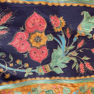 May include: A dark blue fabric with a gold and red floral pattern. The pattern features stylized flowers, leaves, and stems. The fabric has a repeating pattern.