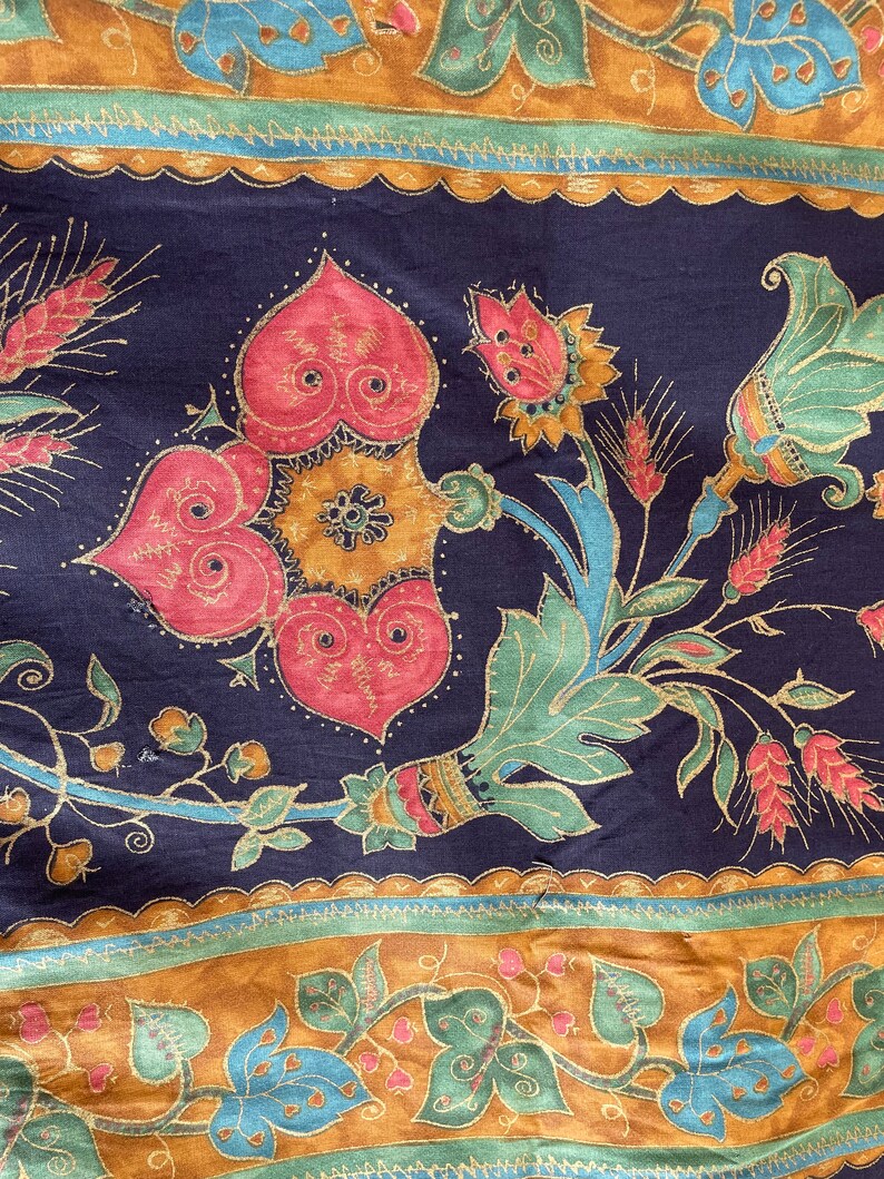 May include: A dark blue fabric with a gold and red floral pattern. The pattern features stylized flowers, leaves, and stems. The fabric has a repeating pattern.