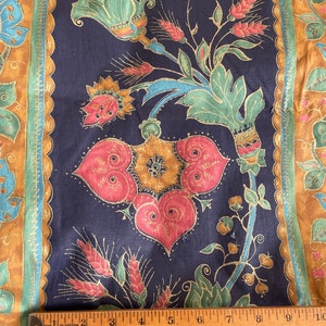 May include: A navy blue fabric with a gold, pink, and green floral pattern. The fabric has a border with a gold, brown, and green pattern. A ruler is placed on the fabric to show the scale.