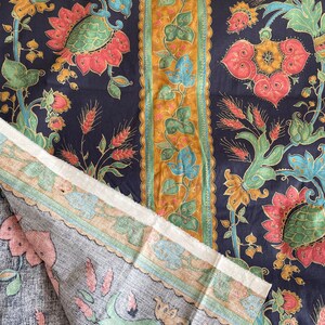 May include: A close-up of two pieces of fabric with a floral pattern. The fabric is dark blue with gold, green, and pink flowers. The fabric is folded over, showing the back side of the fabric, which is a light gray with a similar floral pattern.