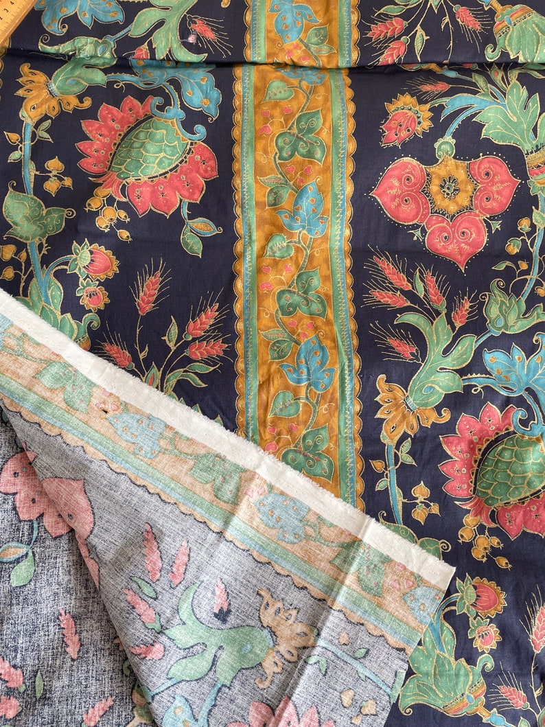 May include: A close-up of two pieces of fabric with a floral pattern. The fabric is dark blue with gold, green, and pink flowers. The fabric is folded over, showing the back side of the fabric, which is a light gray with a similar floral pattern.