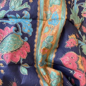 May include: A blue fabric with a repeating pattern of pink, green, and gold floral designs. The fabric has a border with a gold and brown pattern.