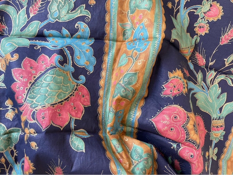 May include: A blue fabric with a repeating pattern of pink, green, and gold floral designs. The fabric has a border with a gold and brown pattern.