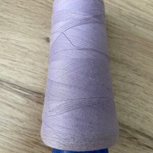 May include: A spool of lavender-coloured thread with a blue plastic bobbin. The thread is wound tightly and has a slightly textured surface.