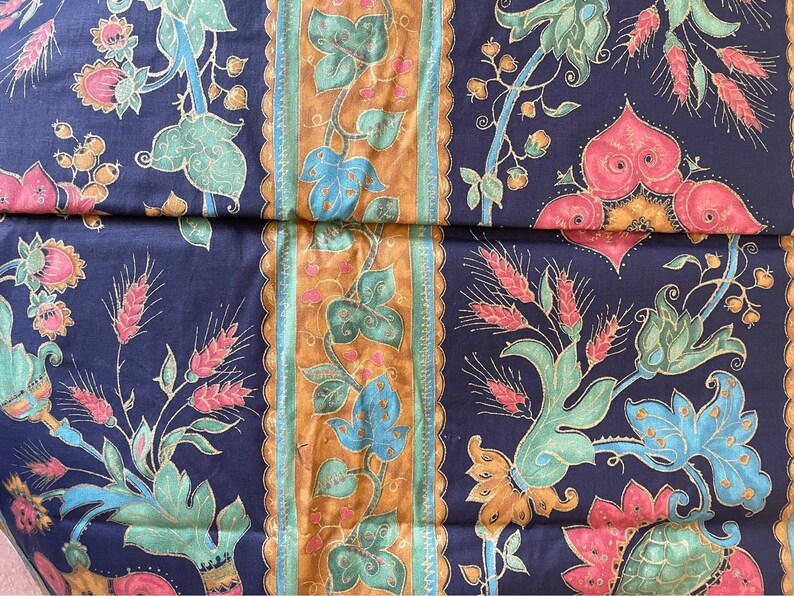 May include: A dark blue fabric with a repeating pattern of gold, green, and pink floral designs. The fabric has a vintage feel and would be perfect for upholstery or quilting.