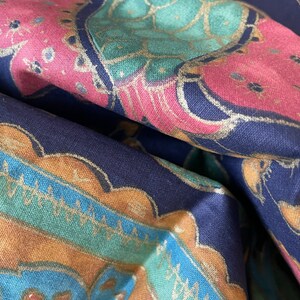 May include: A close-up of a dark blue fabric with a colorful paisley pattern. The fabric features a repeating design of gold, teal, pink, and blue colors.