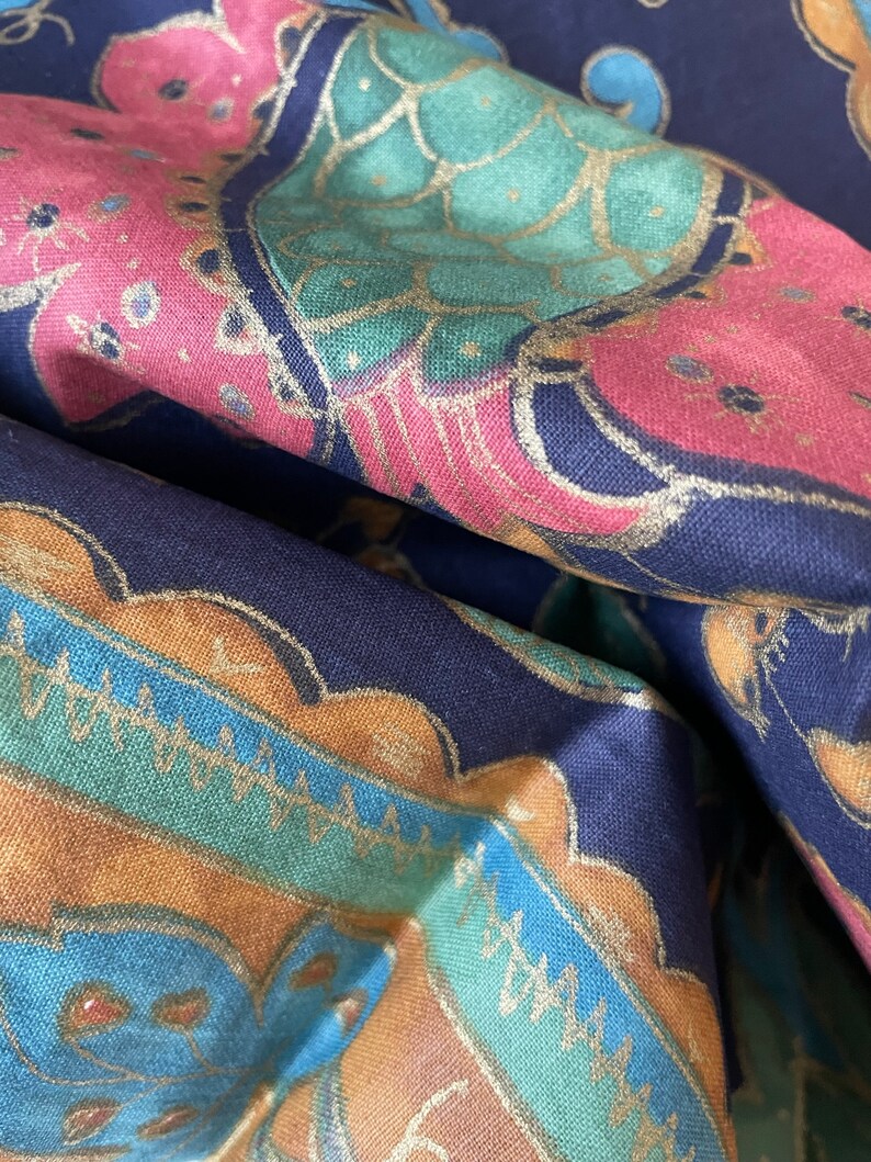 May include: A close-up of a dark blue fabric with a colorful paisley pattern. The fabric features a repeating design of gold, teal, pink, and blue colors.