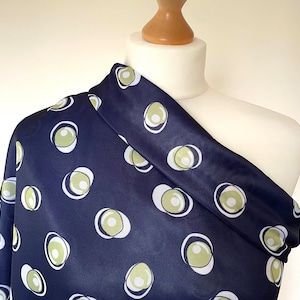 May include: A navy blue fabric with a white and green abstract pattern of circles. The fabric is draped over a white dress form.