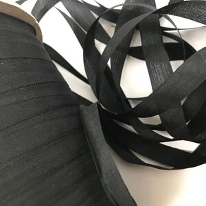 May include: A spool of black elastic ribbon with a textured surface. The ribbon is folded and coiled on a white surface.