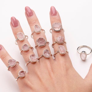 May include: A hand model wearing a variety of rings featuring pink rose quartz gemstones set in silver.