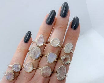 Op de afbeelding: Een handmodel draagt ​​verschillende zilveren ringen met iriserende maansteen-settings. De ringen zijn gestapeld op meerdere vingers.