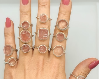 May include: A hand model wearing a variety of rings featuring pink rose quartz gemstones set in silver.