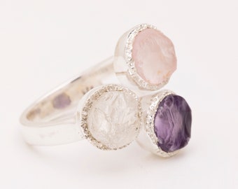 Op de afbeelding: Een zilveren ring met drie bezel-gezet edelstenen: een heldere kwarts, een roze rozenkwarts en een paarse amethist.