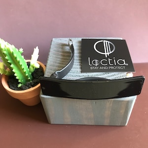 May include: Black wristband with a silver clasp and the text "loctia. STAY AND PROTECT" on a white card. The wristband is on a wooden block.