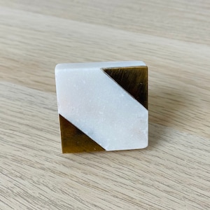 May include: Square cabinet knob with a white marble and gold design. The marble is white with gray veining. The gold is a solid color.