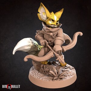 May include: A miniature figurine of a fox-like creature with large ears, wearing a hooded cloak and holding a bow and arrow. The figurine is painted in shades of brown and yellow, with a white tail.