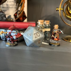 May include: A silver 20-sided die with white numbers, a miniature red dragon figurine, and a miniature red and gold warrior figurine with a pickaxe.