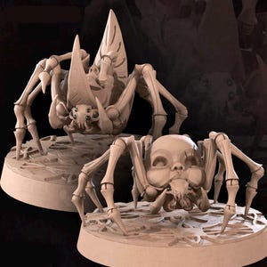 May include: Two beige-colored, stylized spider sculptures. Each spider has a unique design, with a skeletal appearance and intricate details. They are positioned on circular bases with a textured surface, creating a fantasy or gothic theme.