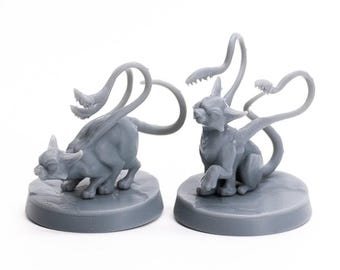 May include: Two gray fantasy creature figurines. One is posed low to the ground, the other is seated. Each has a cat-like body, horns, and a long, tentacle-like appendage with a toothed mouth.