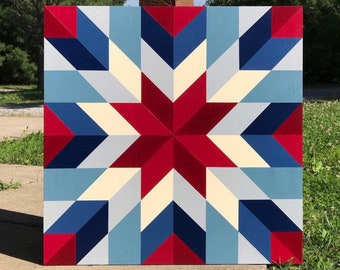 May include: A red, white, and blue barn quilt with a starburst design. The quilt is painted on a wooden board and has a geometric pattern.