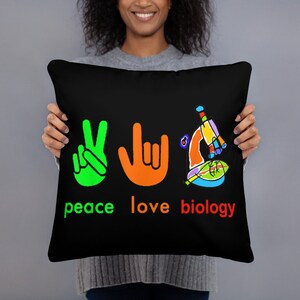 May include: Black throw pillow with the words "peace love biology" in colorful text. The design includes a green peace sign, an orange hand making a rock on gesture, and a colorful illustration of a microscope.